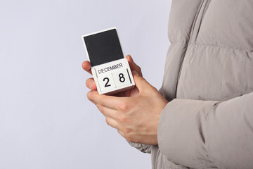 Man in down jacket holds wooden block calendar with date December 28