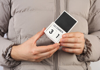 Man in down jacket holds wooden block calendar with date December 31