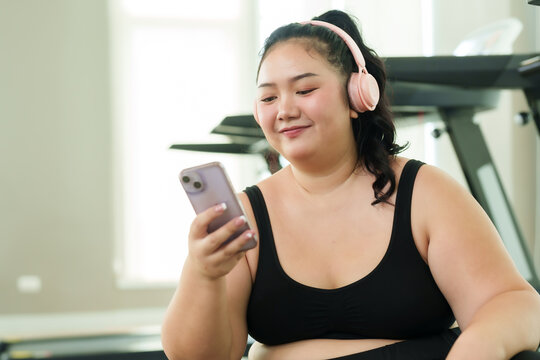 Close-up of half body of chubby woman sitting wearing headphones. Listen to music in the fitness center The happiness of a cute fat Asian girl Sway to the rhythm of the music after exercising.