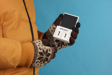 Man in yellow winter down jacket and gloves holding block calendar with date january 11 on blue background
