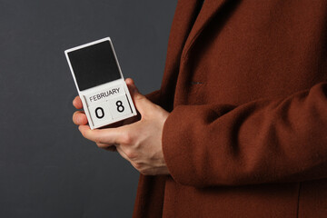 Man in woolen coat holds calendar with the date february 8