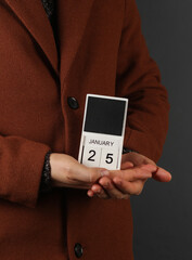 Man in woolen coat holds calendar with the date february 25