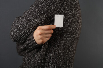 Man in a sweater holds a white tag on dark gray background