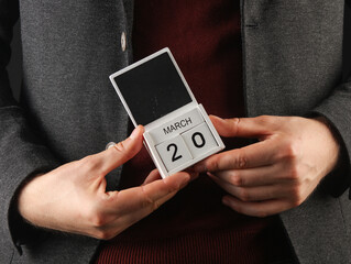 Business man in a jacket holding a calendar with the date March 20