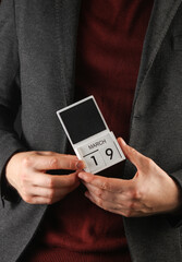 Business man in a jacket holding a calendar with the date March 19