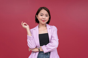 A modern young and smart asian woman in her mid 20s sporting short hair. Wearing a pink blazer and black tube top. Studio shot with burgundy background.