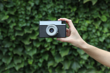 Retro film camera in woman’s hand against the green leaves wall background