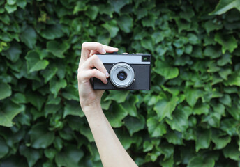 Retro film camera in woman’s hand against the green leaves wall background