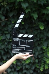 Movie clapperboard in woman’s hand against the green leaves wall background