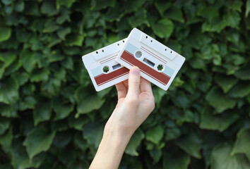 Hand holding retro 80s audio cassettes on green leaves wall background