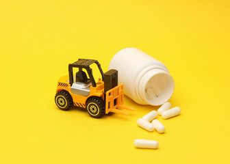 Miniature toy forklift and pills on a yellow background. Logistics, medicines delivery