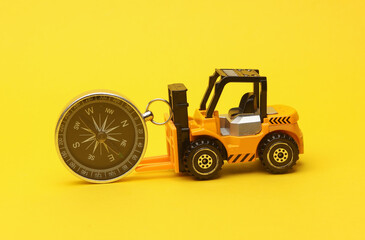 Miniature toy forklift and compass on a yellow background. Logistics, transportation, delivery