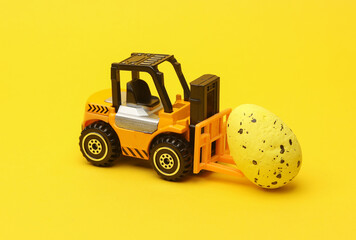 Miniature toy forklift and easter egg on a yellow background.