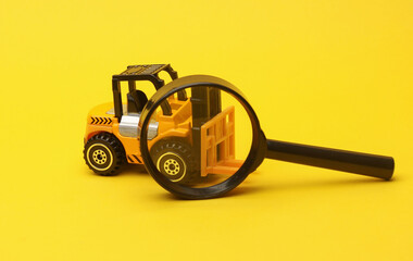 Miniature toy forklift and magnifying glass on a yellow background. Logistics, transportation, delivery © splitov27