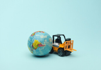 Miniature toy forklift and globe on blue background. Logistics, transportation, delivery