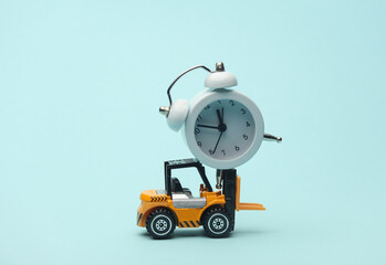 Miniature toy forklift and alarm clock on blue background. Logistics, transportation, delivery