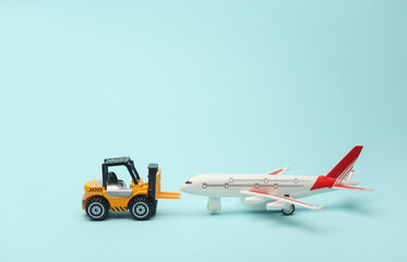 Miniature toy forklift and air plane on blue background. Logistics, transportation, delivery