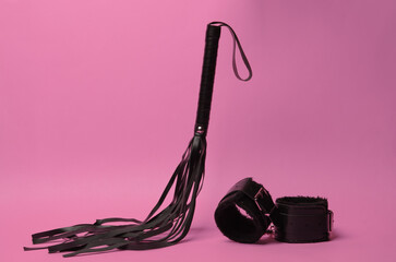 Leather bdsm handcuffs and whip levitating on pink background. Dominance. Sex games.