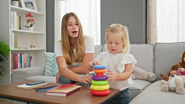 Smiling caucasian mother and daughter sitting comfortably, playing a game on a smartphone, relaxing together at home on the sofa