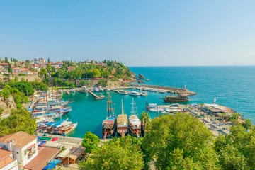 Stoff pro Meter Panoramic view of Antalya, Turkey. Deep blue-green waters of the Mediterranean Sea meet a bustling harbor filled with boats of various sizes. A white lighthouse stands sentinel on a rocky outcropping © bennymarty