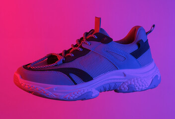 Trendy sport's sneaker floating in the air, isolated in blue-red neon gradient light. Levitating objects. Minimal concept