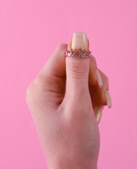 Golden ring in the form of crown with diamonds on female finger. Pink background
