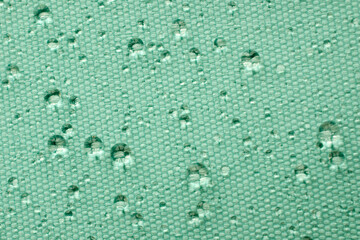 Rainwater drops on turquoise waterproof fabric, top view. Water drops on waterproof soaked fabric in the rain, top view. Water drops on turquoise waterproof fabric.