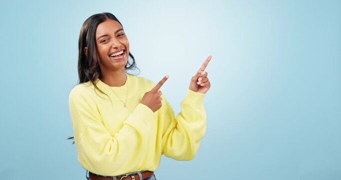 Happy, dance and face of woman with hand pointing in studio for deal, giveaway or promo on blue background. excited, news and portrait of Indian female model show sale, discount or prize announcement