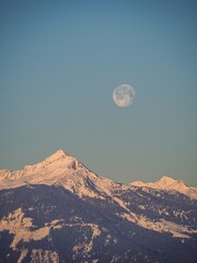 Full moon setting over a snow covered winter mountain peak in the Alps