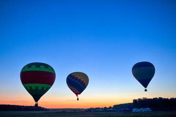 Line of Three Colorful Air Balloons Levitating Over the Field Outdoors Against Clear Blue Skies At Twilight.