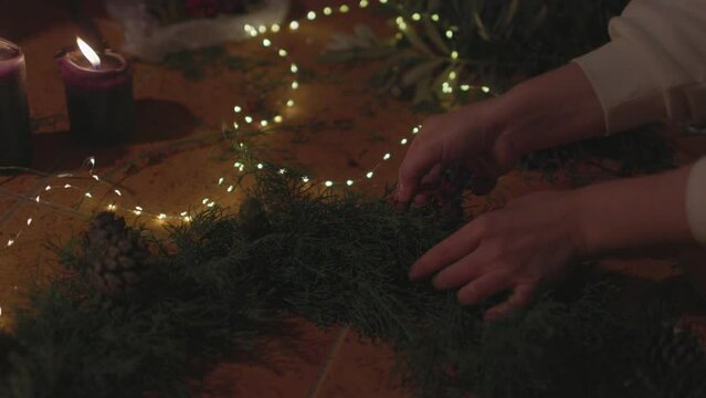 A girl collects New Year's decor. burning candles with Christmas decorations of pine cones around.