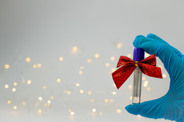 Christmas in laboratory. Hand in blue glow show medical test tubes with christmas bows and...