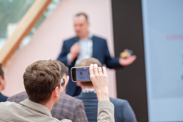 Businessman photographing speaker through smart phone while attending presentation in conference...