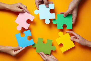Сolored puzzles in hands on orange background, top view - obrazy, fototapety, plakaty