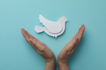 Decorative paper bird and hands on blue background, top view