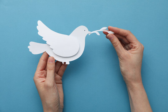 Decorative paper bird in hands on blue background, top view