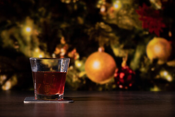 Glass of whiskey on the bar in front of the blur image Christmas home room with tree and festive bokeh lighting, blurred holiday background