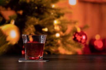 Glass of whiskey on the bar in front of the blur image Christmas home room with tree and festive bokeh lighting, blurred holiday background