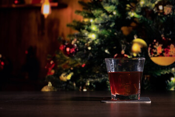 Glass of whiskey on the bar in front of the blur image Christmas home room with tree and festive bokeh lighting, blurred holiday background