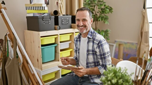 Confident middle-aged man with grey hair, smiling joyfully while drawing in his art studio, celebrating creativity and expertise