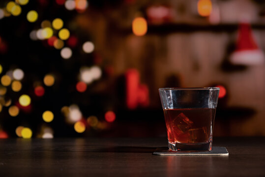 Glass of whiskey on the bar in front of the blur image Christmas home room with tree and festive bokeh lighting, blurred holiday background