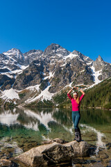 a woman stands and shows a heart by a beautiful lake in the mountains. Famous mountains lake Morskie oko or sea eye lake In High Tatras. Five lakes valley - obrazy, fototapety, plakaty