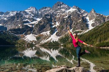 Young girl enjoying beauty of nature looking at mountain lake in famous mountains lake Morskie oko or sea eye lake In High Tatras. Five lakes valley. Adventure travel in Slovekia, Europe. - obrazy, fototapety, plakaty