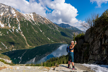 woman standing over the lake and taking a selfie in the mountains, Beautiful Eye of the Sea lake in Tatra mountains, Poland