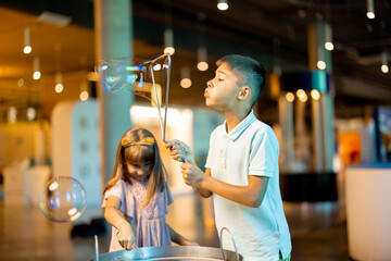 Little girl and boy make soap bubbles, while playing together and having fun in a science museum. Concept of children's entertainment and learning