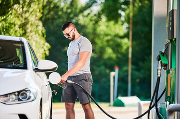 Driver with gasoline pump refilling car gas tank. Confident man refueling his luxury white auto....