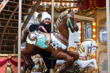 A woman in a winter fur coat rides a carousel in the winter park on the square. New Year's walk...