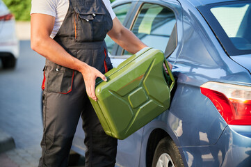 Stalled car filling with gasoline by professional worker. Young man refueling gas tank with fuel...