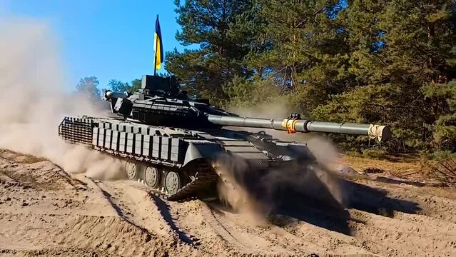 A tank with a Ukrainian flag drives near the forest on the sand, picking up sand, and turns around. A real battle, an offensive. Russian-Ukrainian war.