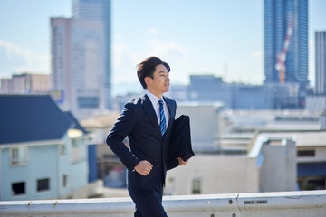 カバンを持って走るスーツを着た若い日本人ビジネスマン
